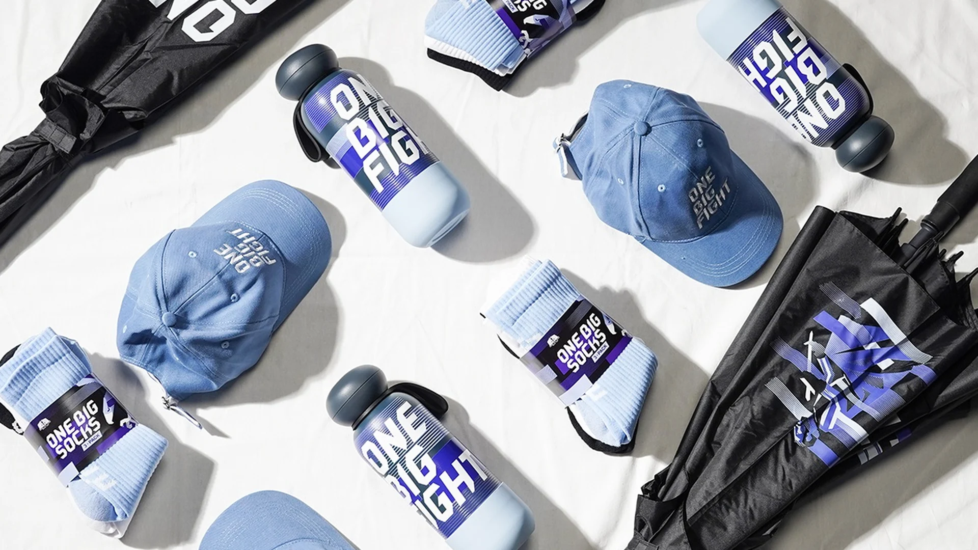 Caps, socks, flasks and umbrellas from the first One Big Fight merch drop, laid out on white linen